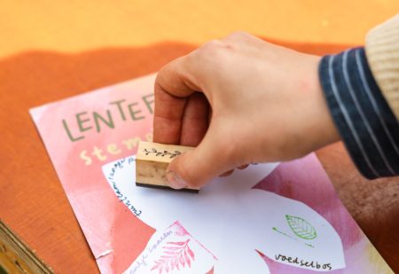 een hand met een stempel die stempelt op een papier met daarop bijna helemaal leesbaar 'lentefestival'